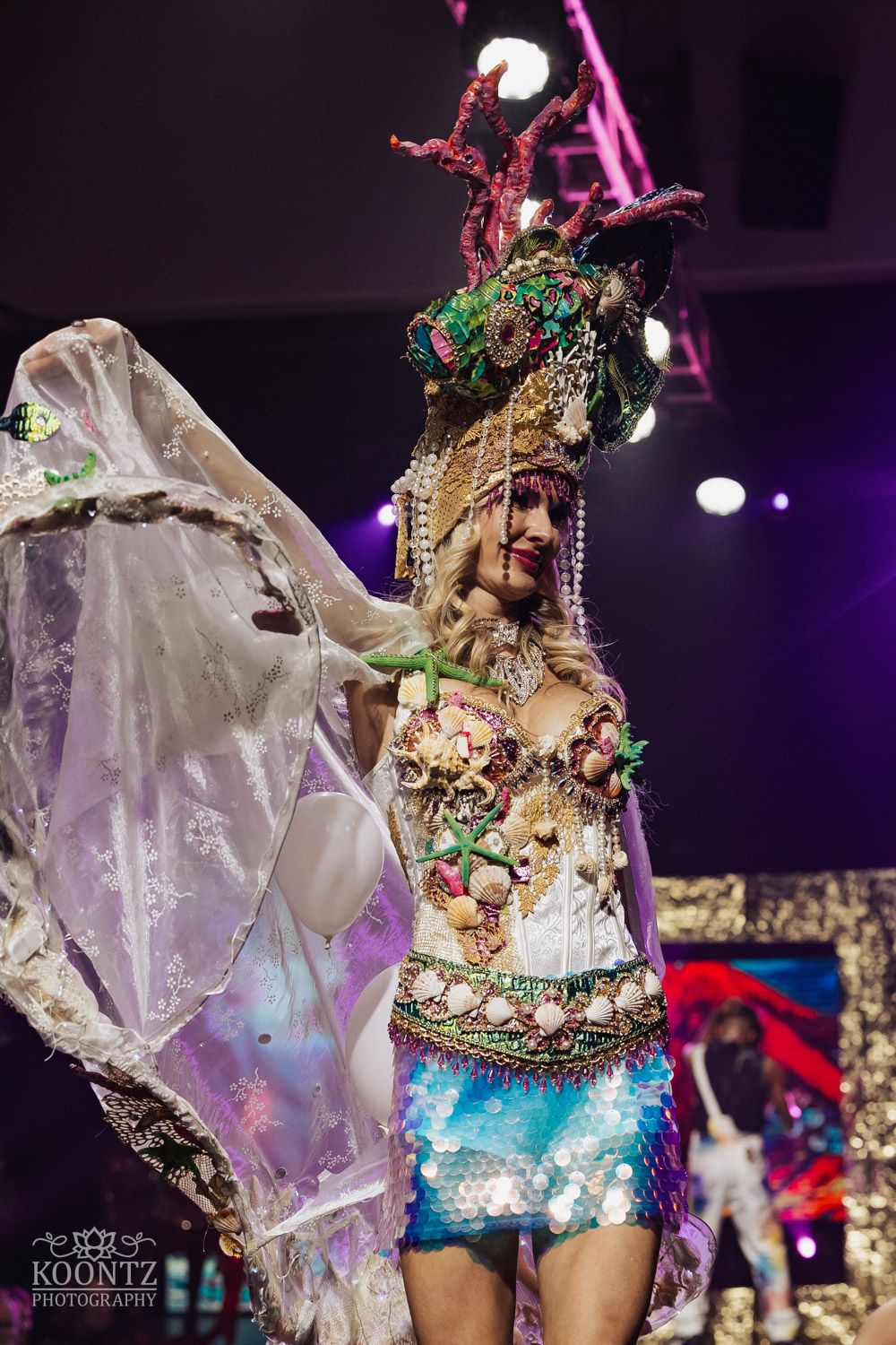 Dancers in sparkly costumes with flowy fabric perform under colorful stage lighting at an entertainment show.