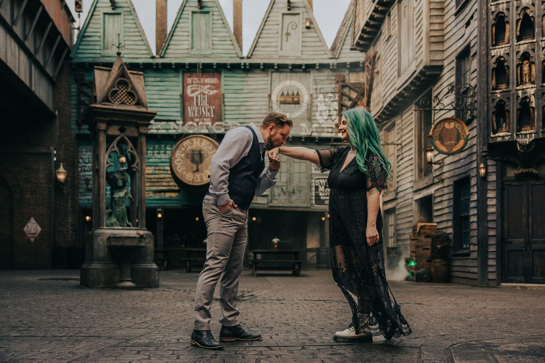 Man gallantly kissing womans hand with green hair on Diagon Alley cobblestone street.