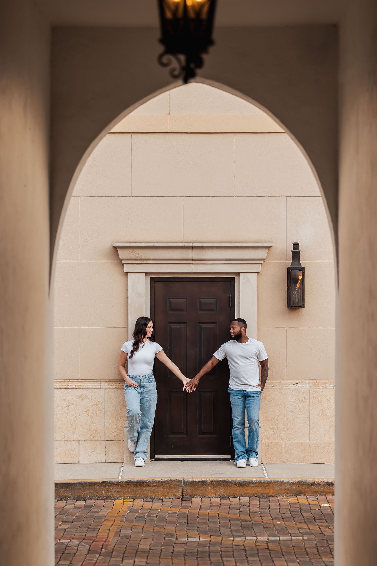 Interracial couple holding hands in front of a brown door framed by an elegant arch.