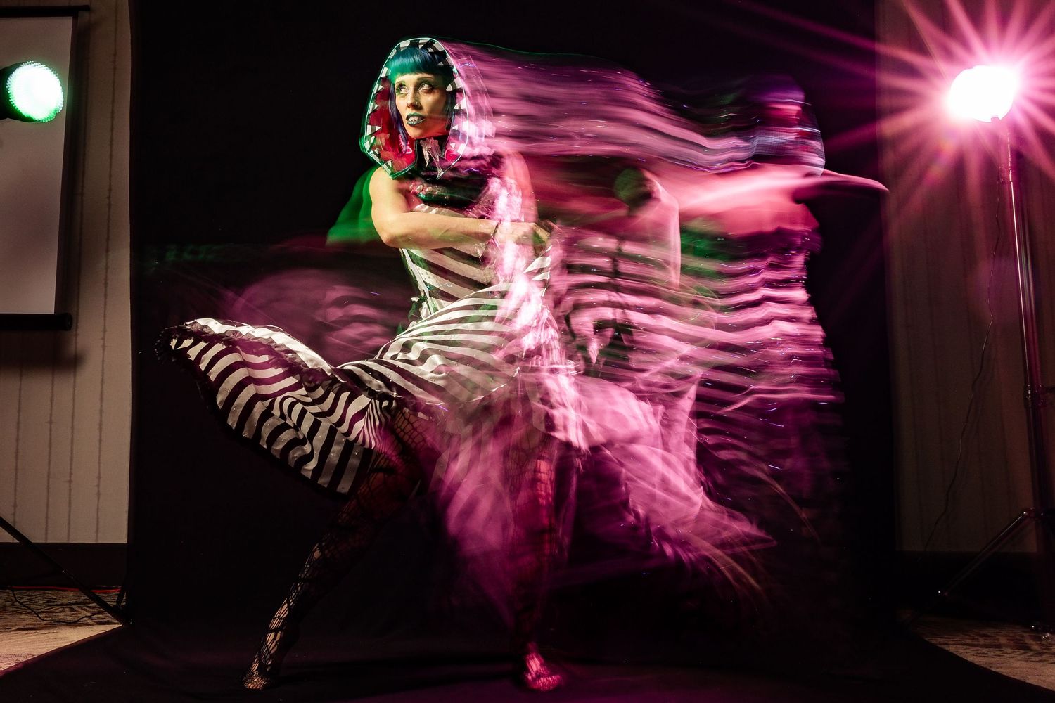 Dancer in zebra-print dress with pink motion blur light trails performing on stage under spotlight.