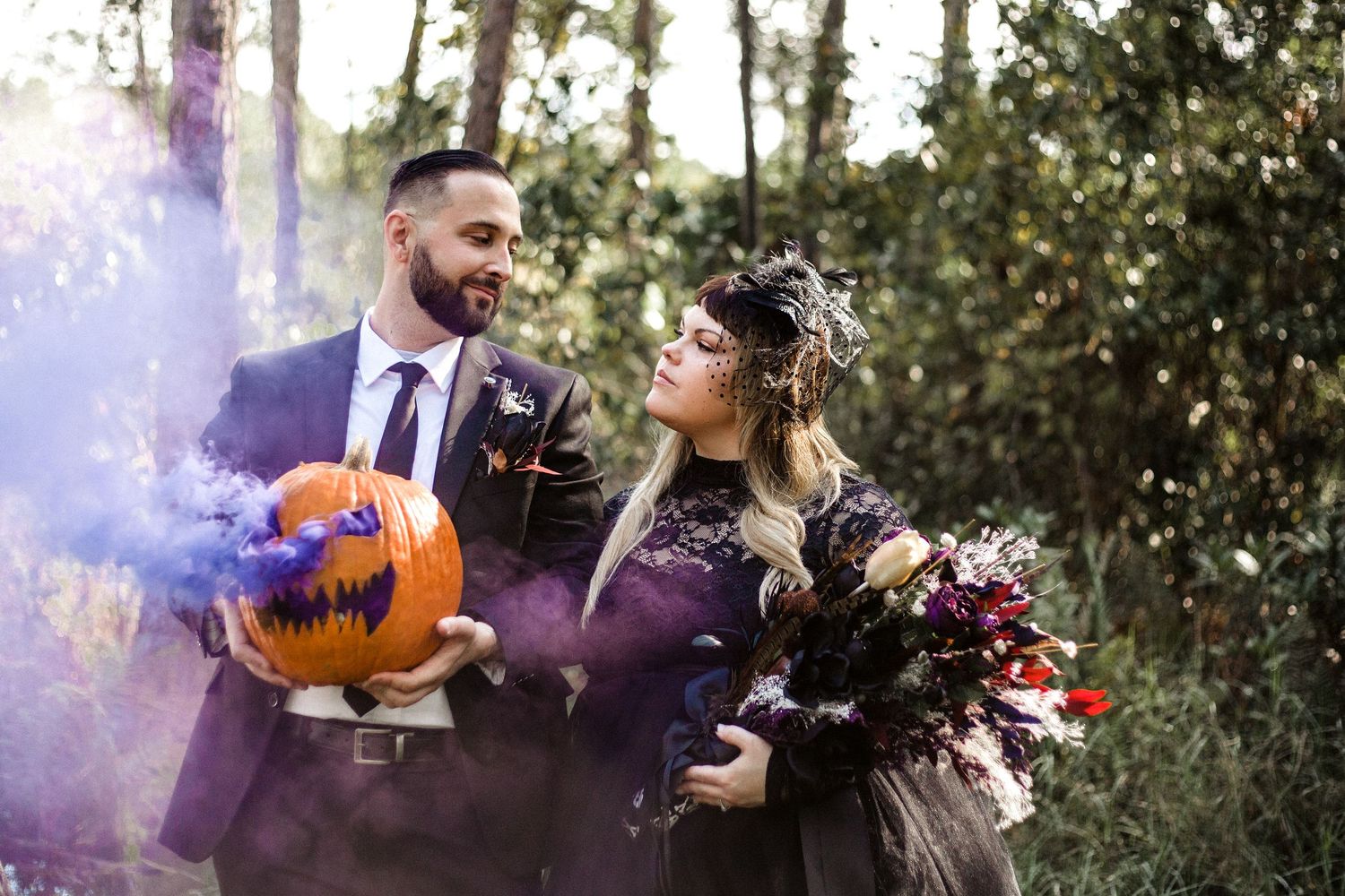 Halloween wedding couple sharing a moment with purple smoke bomb and carved pumpkin outdoors.