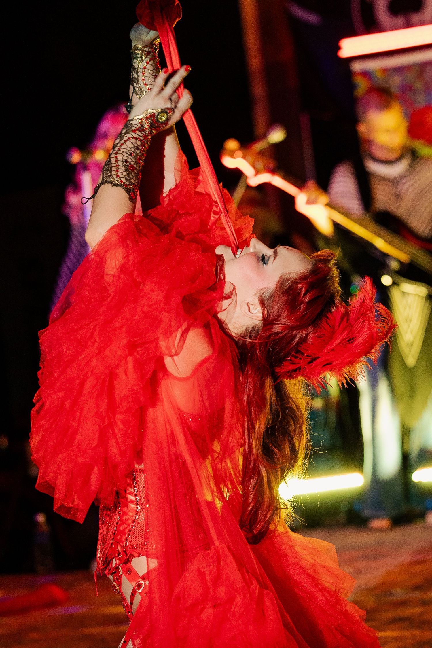 Performer in red feathered gown dramatically arching backward during a theatrical stage performance.