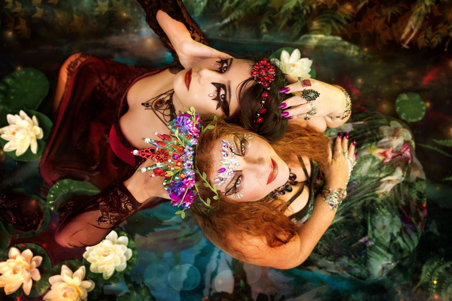 Two women with jeweled makeup and floral crowns pose face-to-face surrounded by water lilies in a fantasy setting.