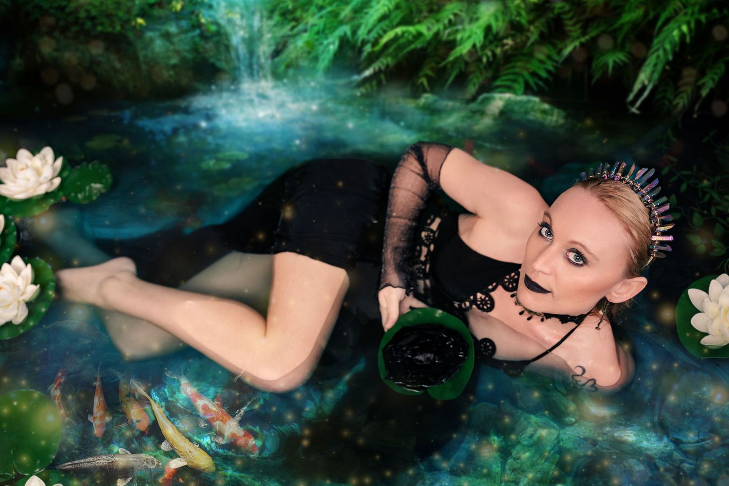 Blonde woman in black dress reclines in mystical koi pond with water lilies in enchanted forest.