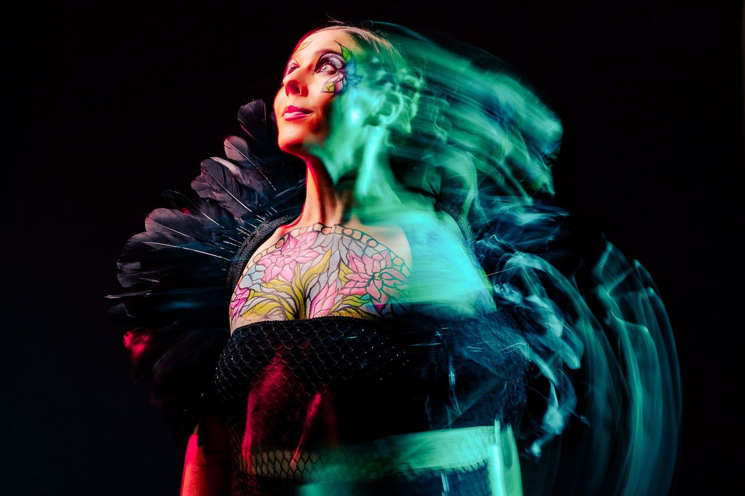 Long exposure portrait of tattooed woman in black ruffled collar with green light blur effect.