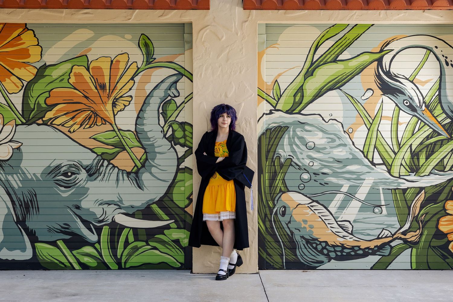 Woman in yellow dress poses before vibrant elephant and koi fish mural street art.