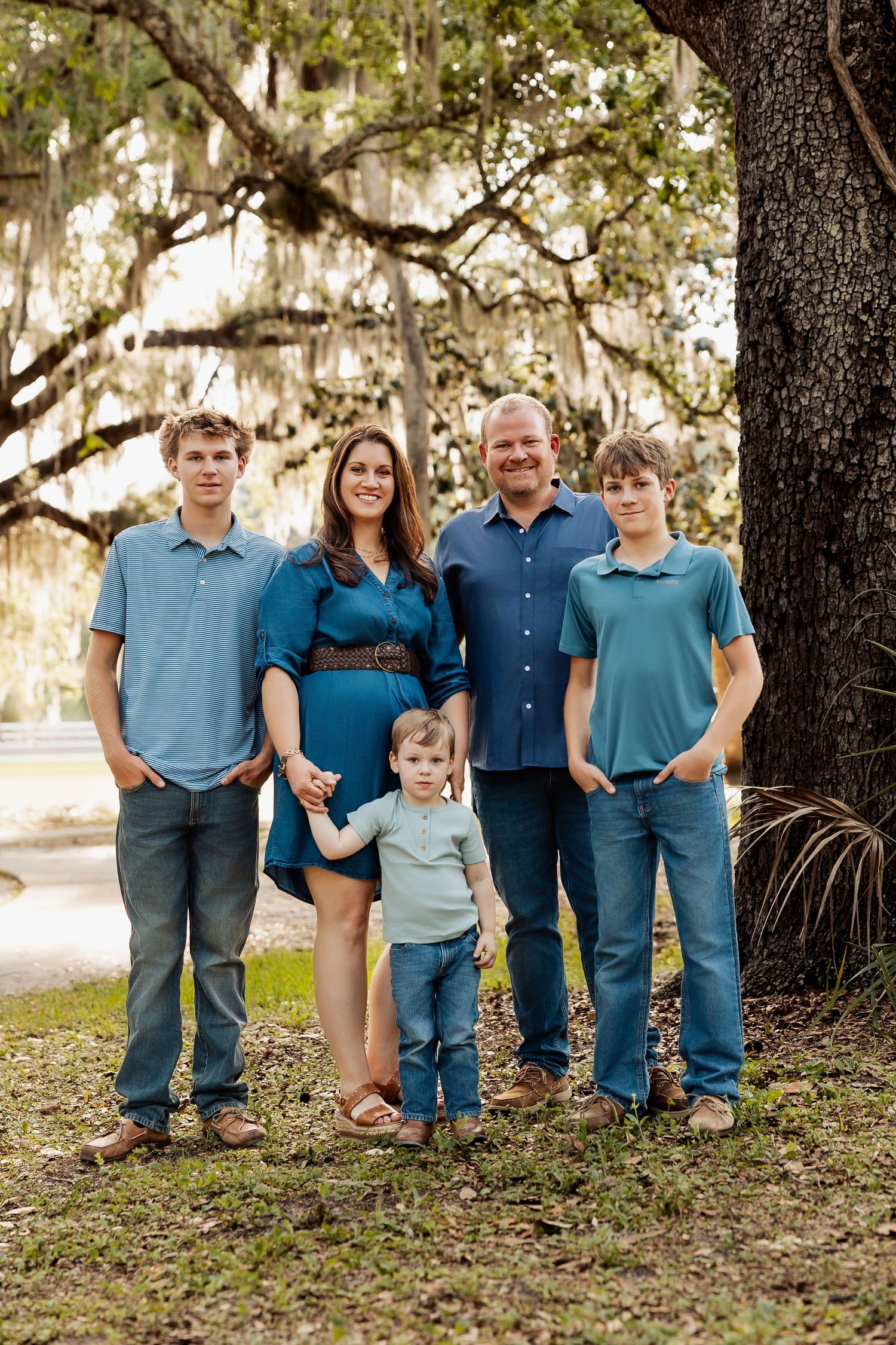 Happy family of five posing under a large oak tree with Spanish moss outdoors.
