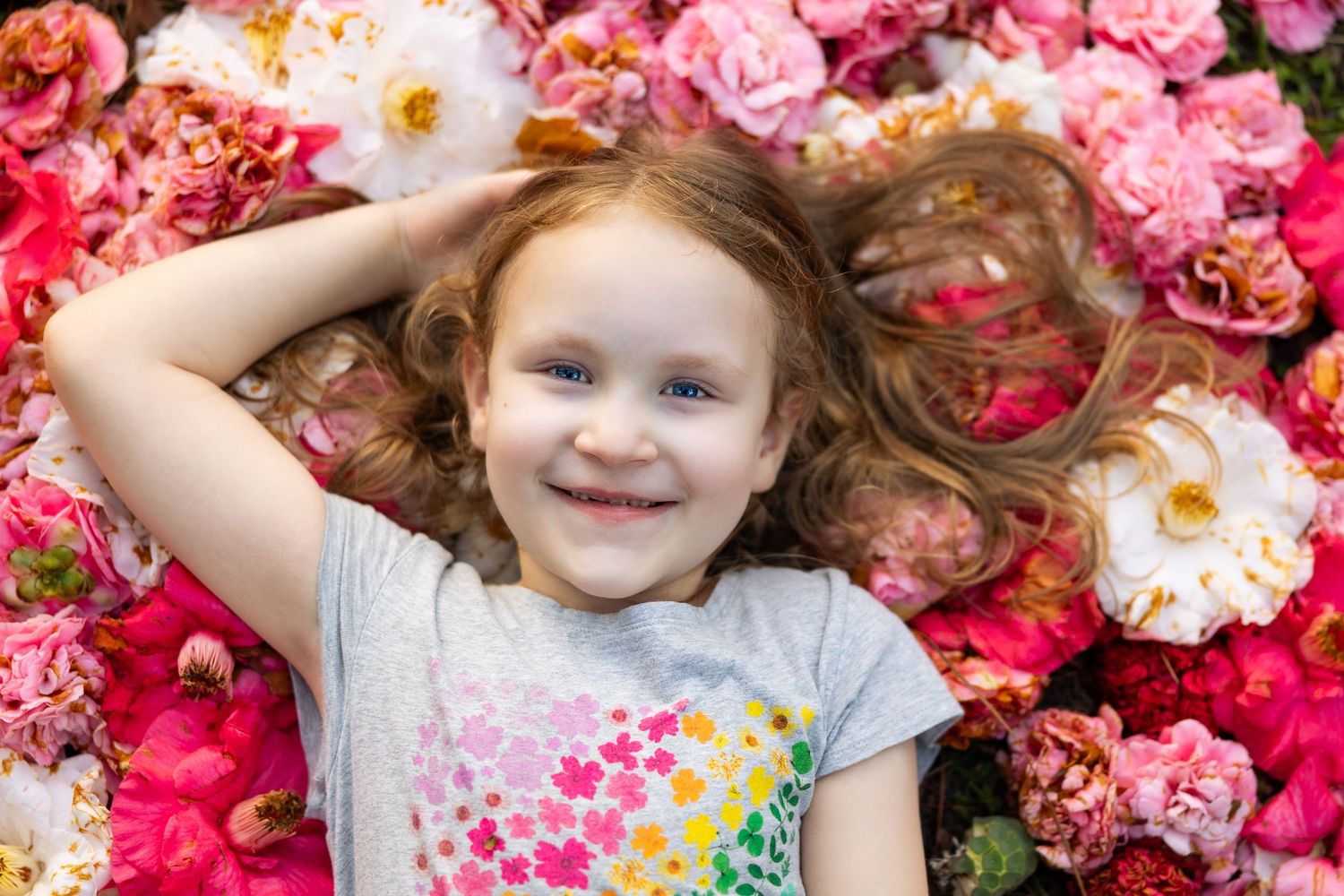 Smiling little girl with red hair lying among colorful pink and white flowers.