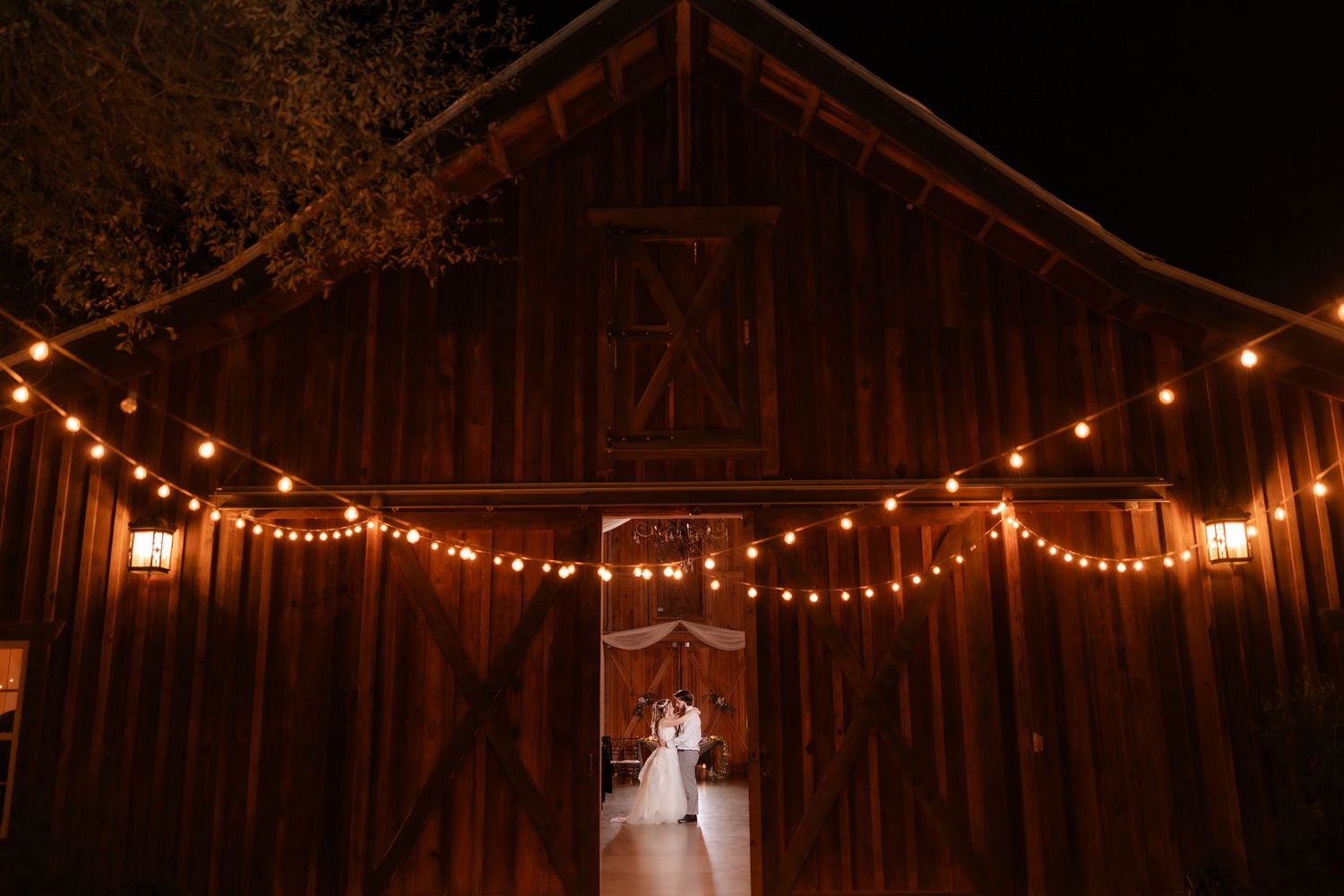 Silhouette of couple in barn doorway with romantic string lights overhead.
