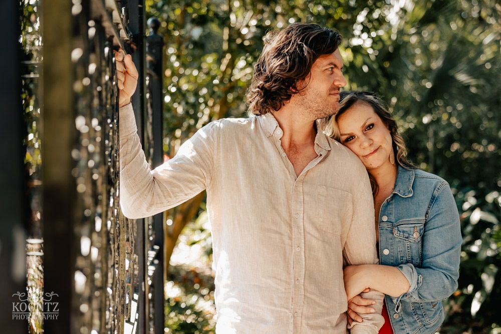 Romantic couple in casual attire embracing against a sunlit natural backdrop with trees.