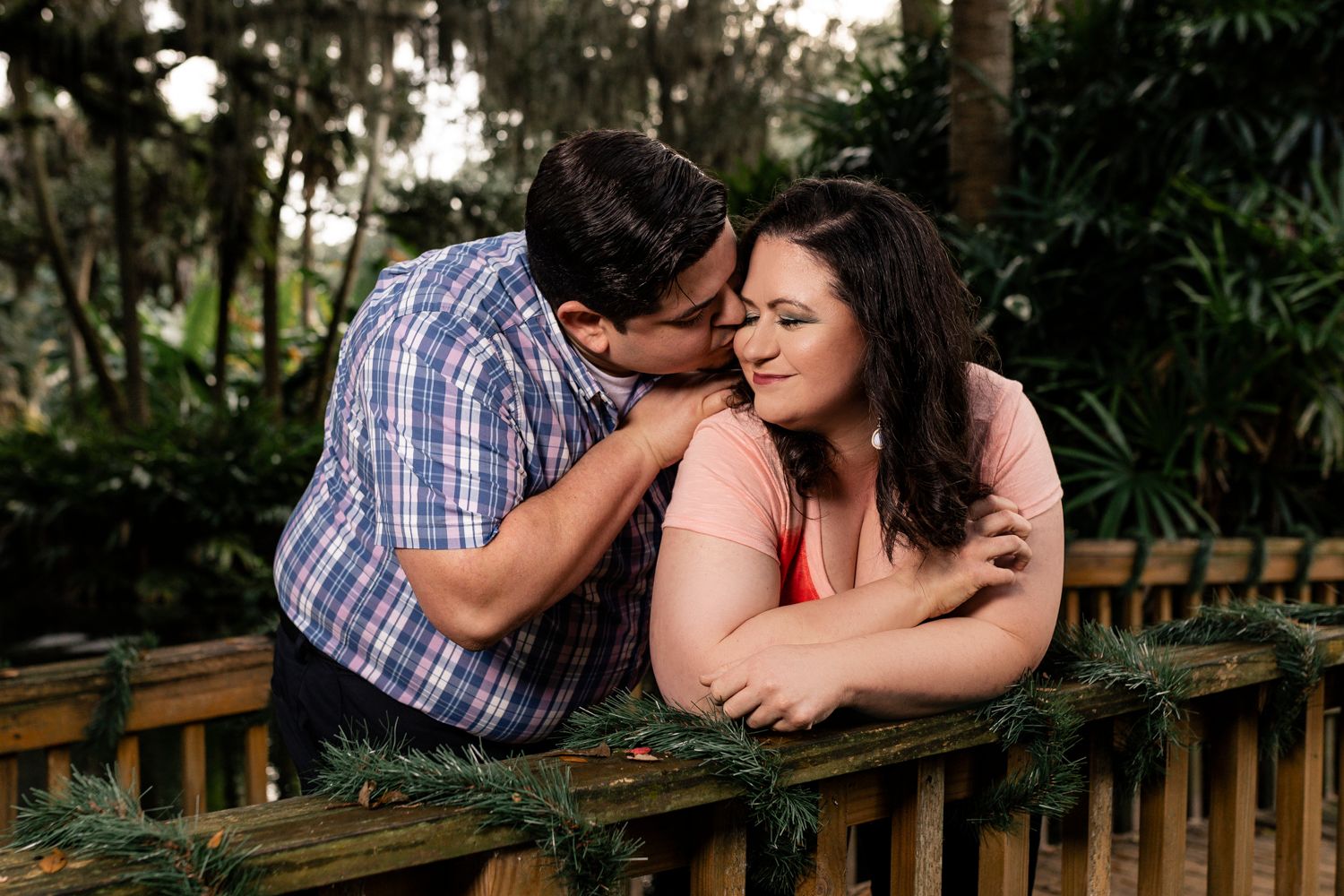 Couple sharing tender moment on wooden bench in lush tropical garden setting.