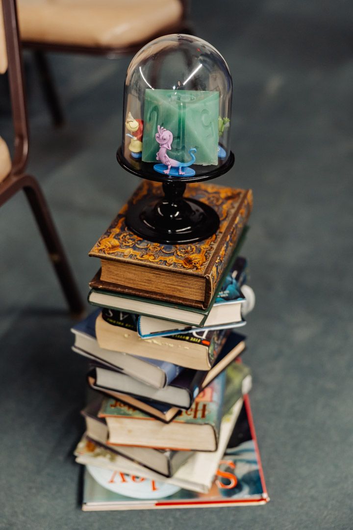 A small glass dome display with green backdrop sits on pile of antique books.