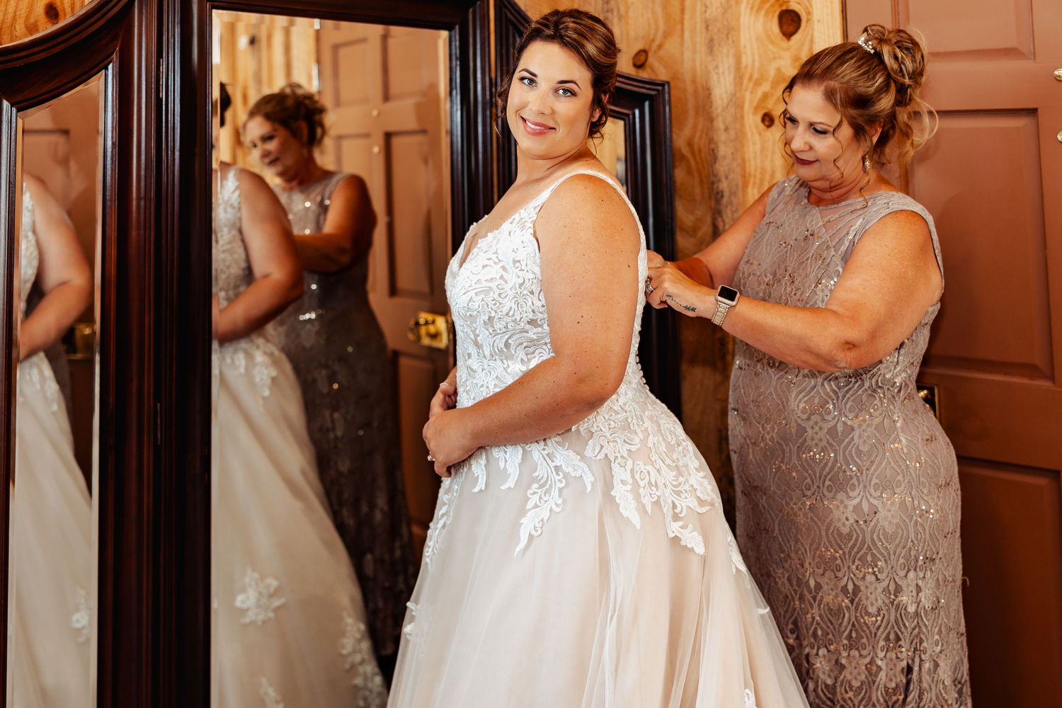 Wedding preparation scene showing dress fitting in rustic wooden room.
