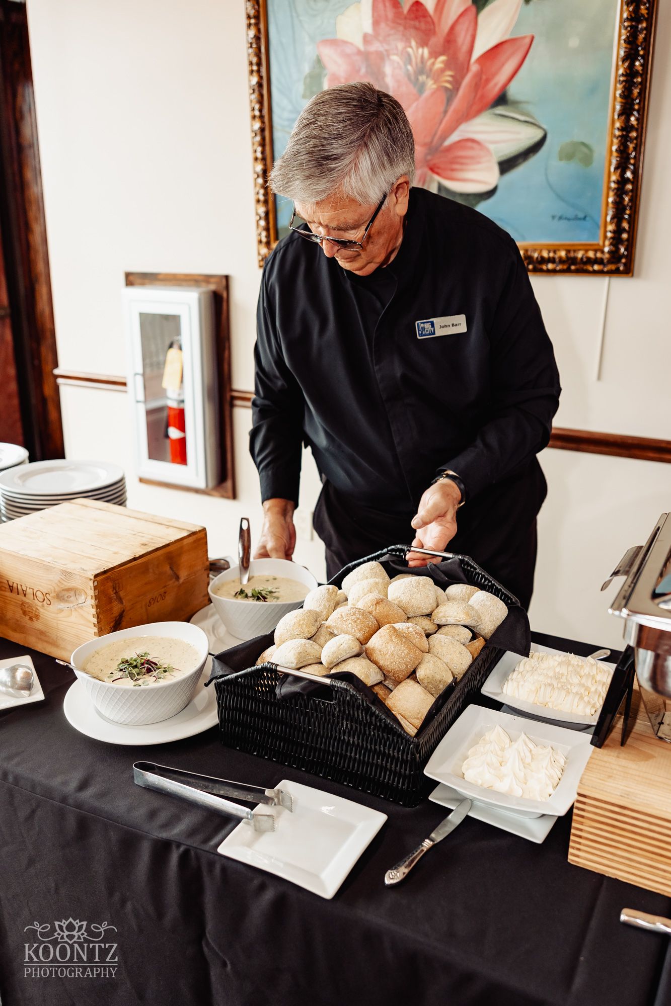 Catering staff member preparing rolls at elegant wedding buffet with framed artwork in background.