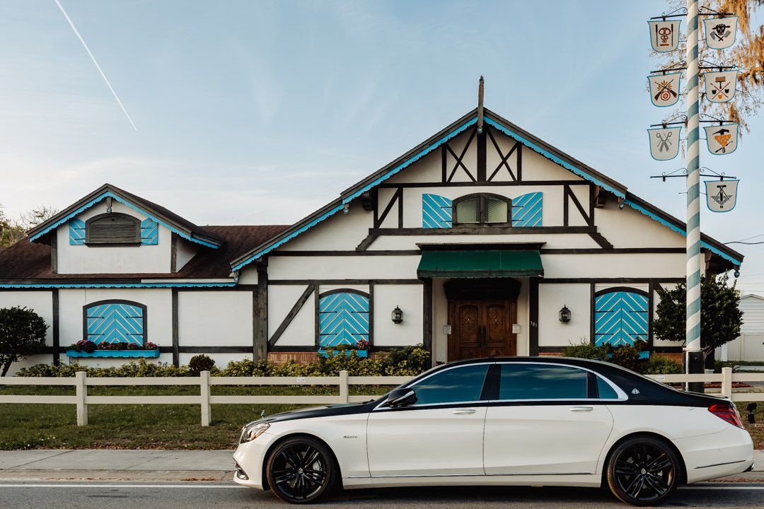 White Mercedes sedan parked outside Tudor-style wedding venue with teal chevron accents.