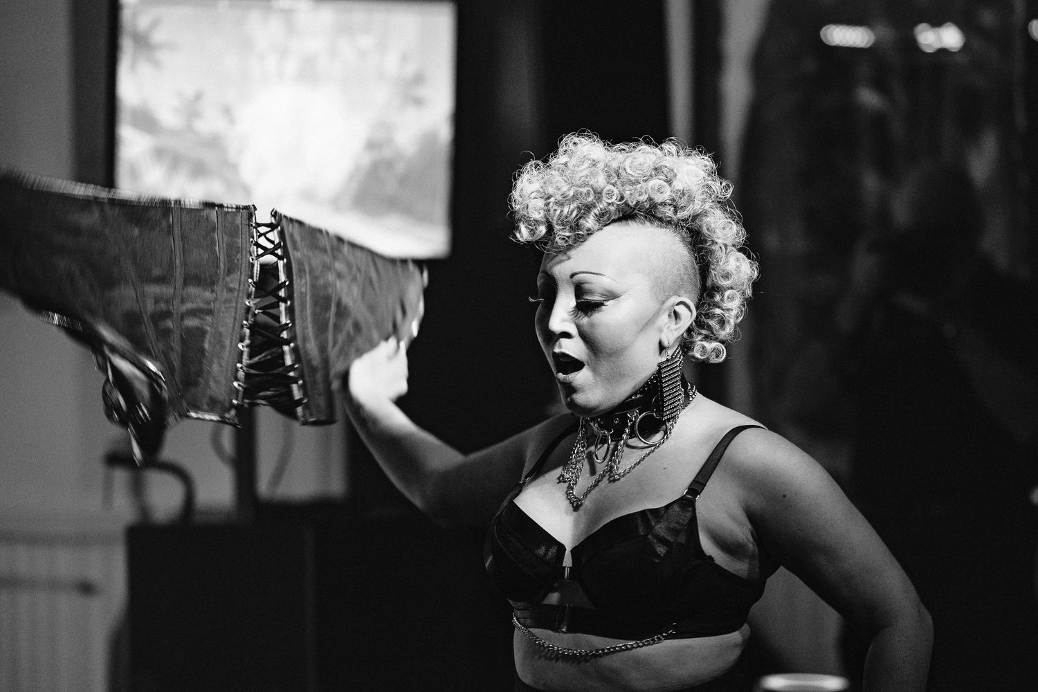 Black and white photo of a woman with blonde mohawk performing on stage in lingerie.