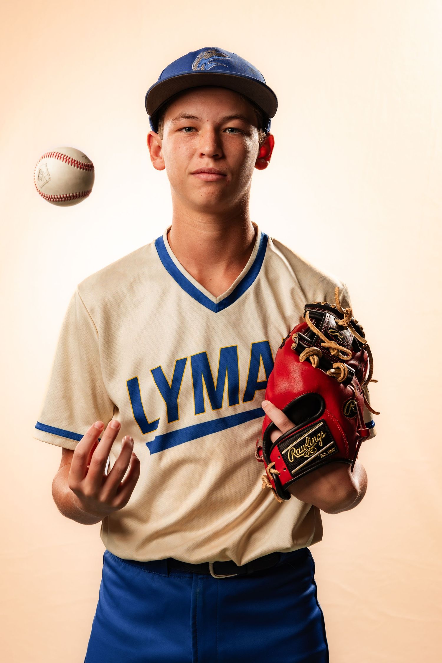Young baseball player in Lyman jersey tossing a ball while holding a Rawlings glove against a neutral background.