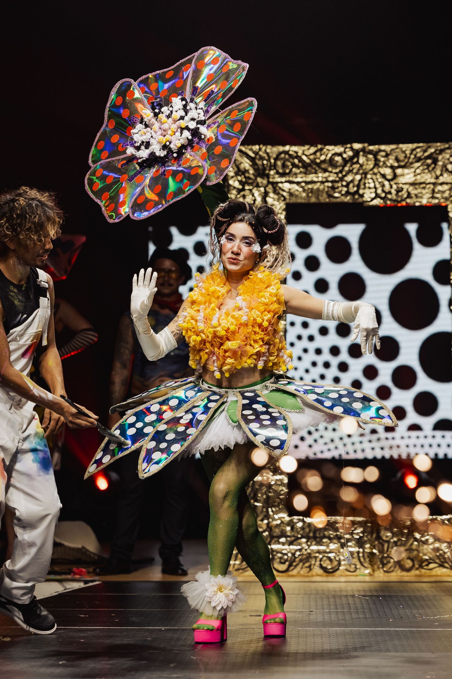 Performer in colorful floral costume with polka dot skirt on stage.