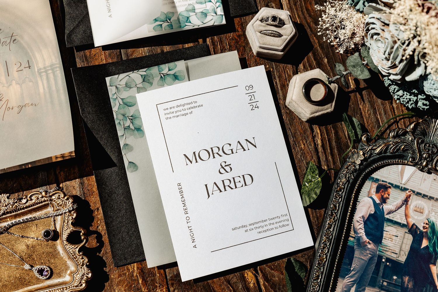 Wedding invitation suite for Morgan and Jared with greenery accents displayed on a rustic wooden surface.