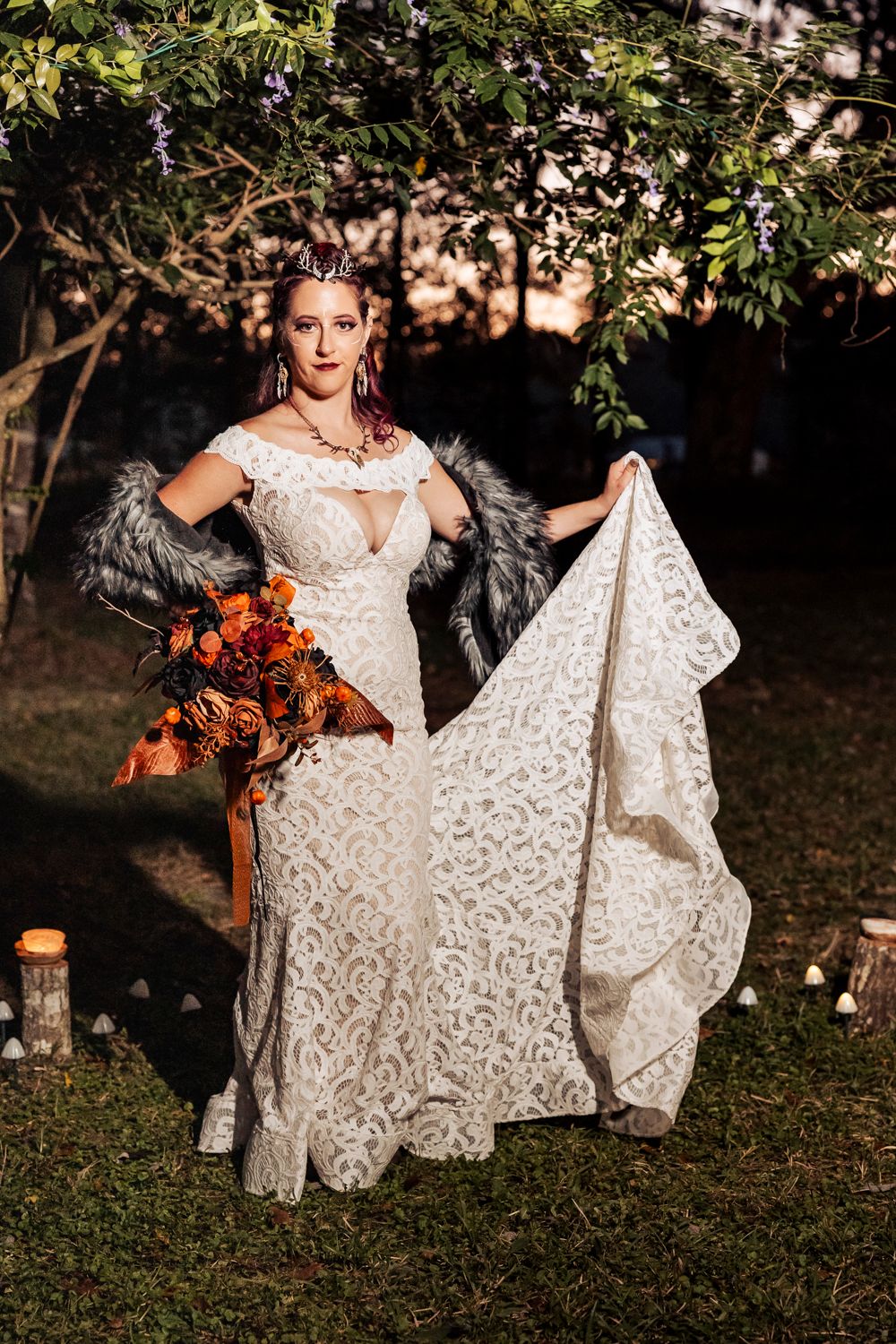 A gothic-inspired wedding photoshoot features a detailed lace gown and dramatic fur accents amidst garden lanterns at dusk.