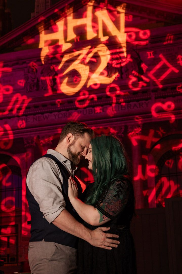 Couple embracing romantically beneath the glowing red HHN 32 Halloween Horror Nights projection.