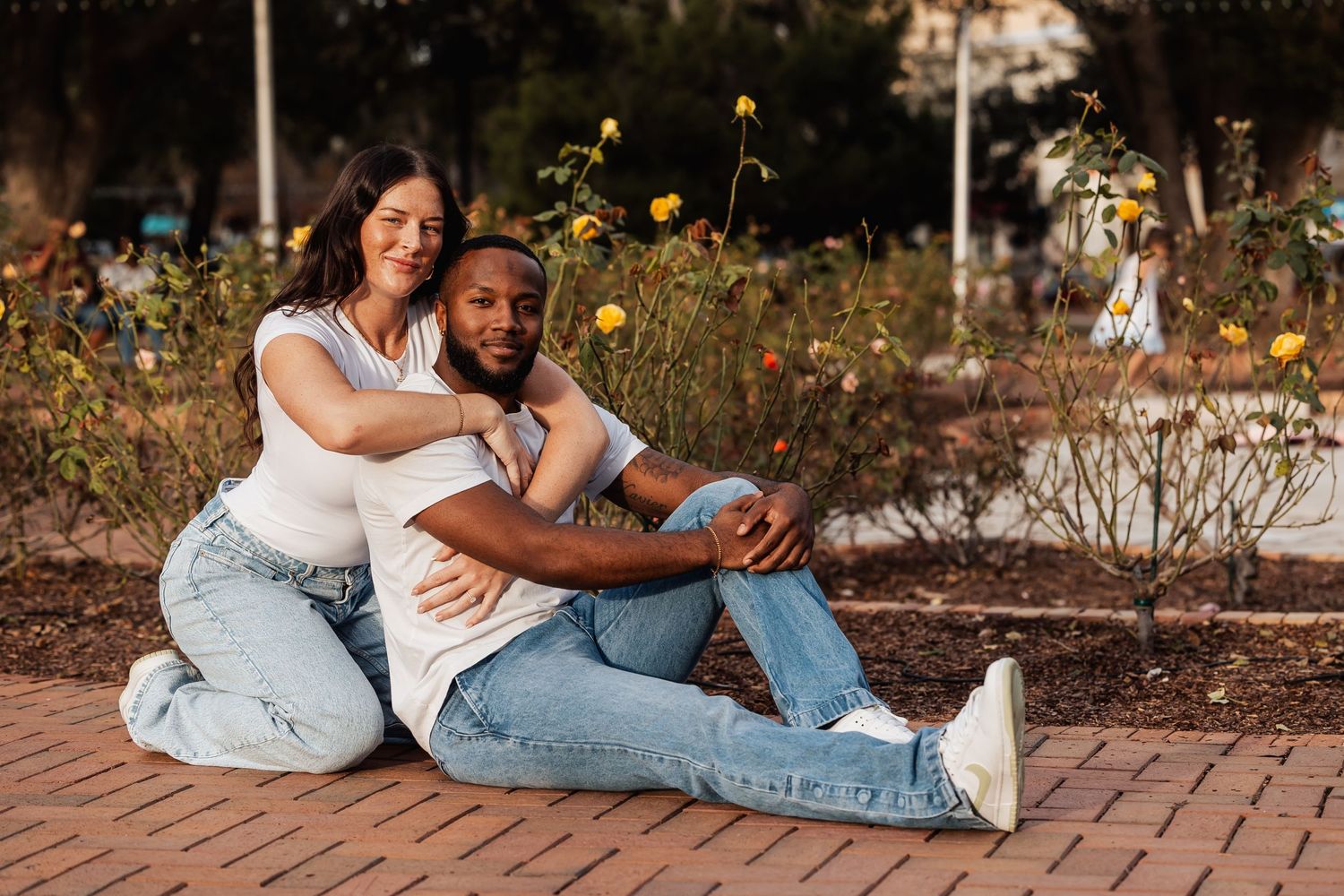 A couple shares a tender moment sitting together among wildflowers on a brick pathway.
