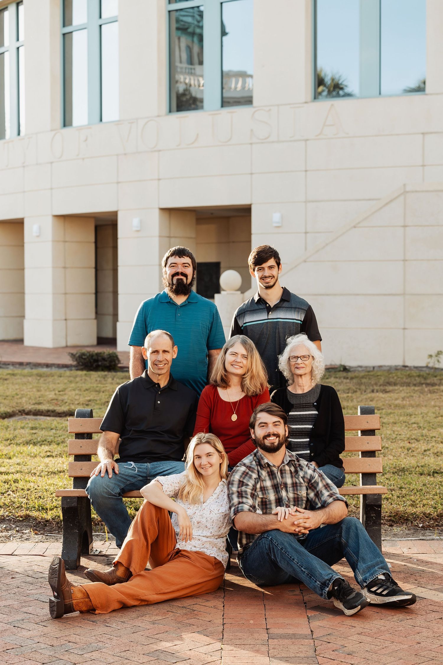 Multigenerational family of seven posing on benches outside a public building.
