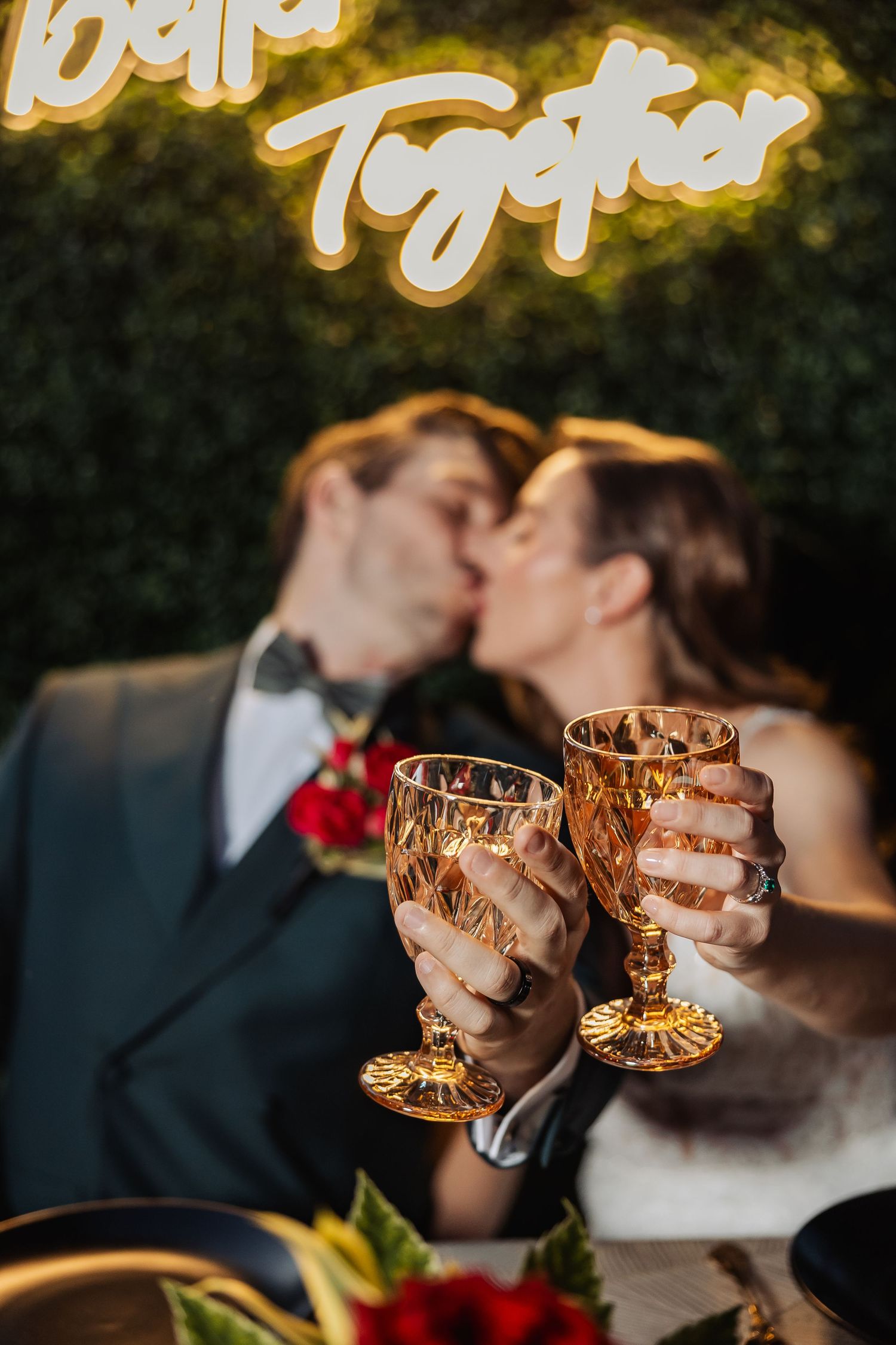 Bride and groom kissing while clinking ornate gold champagne glasses.