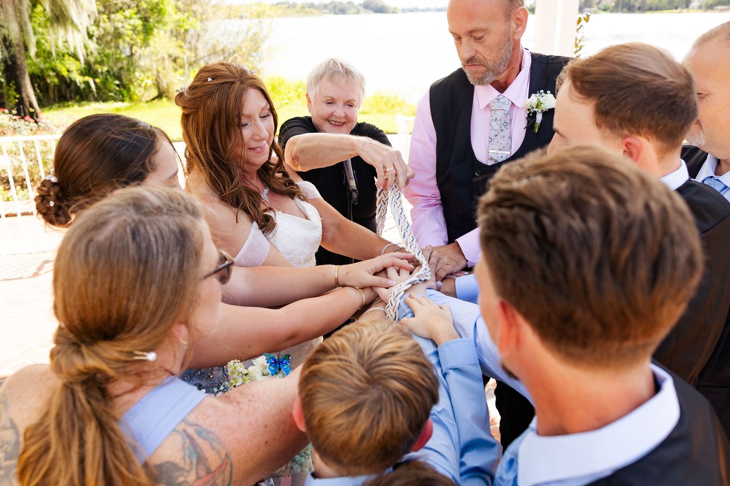 Wedding party participates in a unity ceremony, joining hands together in a joyful outdoor celebration.