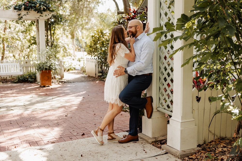 A couple embraces on a sunlit porch with white columns and lattice details.