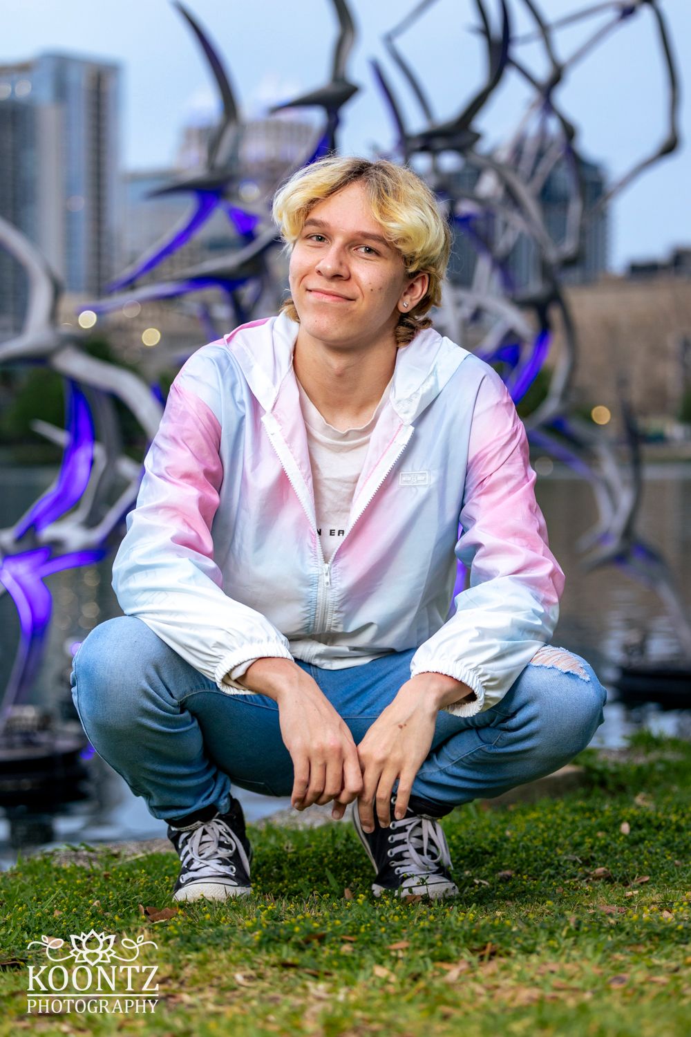 Urban portrait with pastel windbreaker against modern art sculpture backdrop.