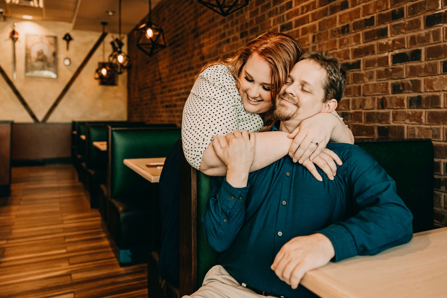Affectionate couple sharing tender moment in restaurant booth with brick wall background.
