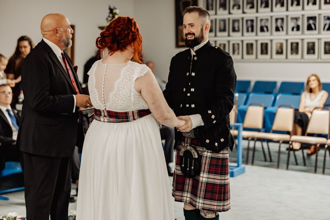 A wedding ceremony in progress showing participants in formal attire including Scottish kilts.