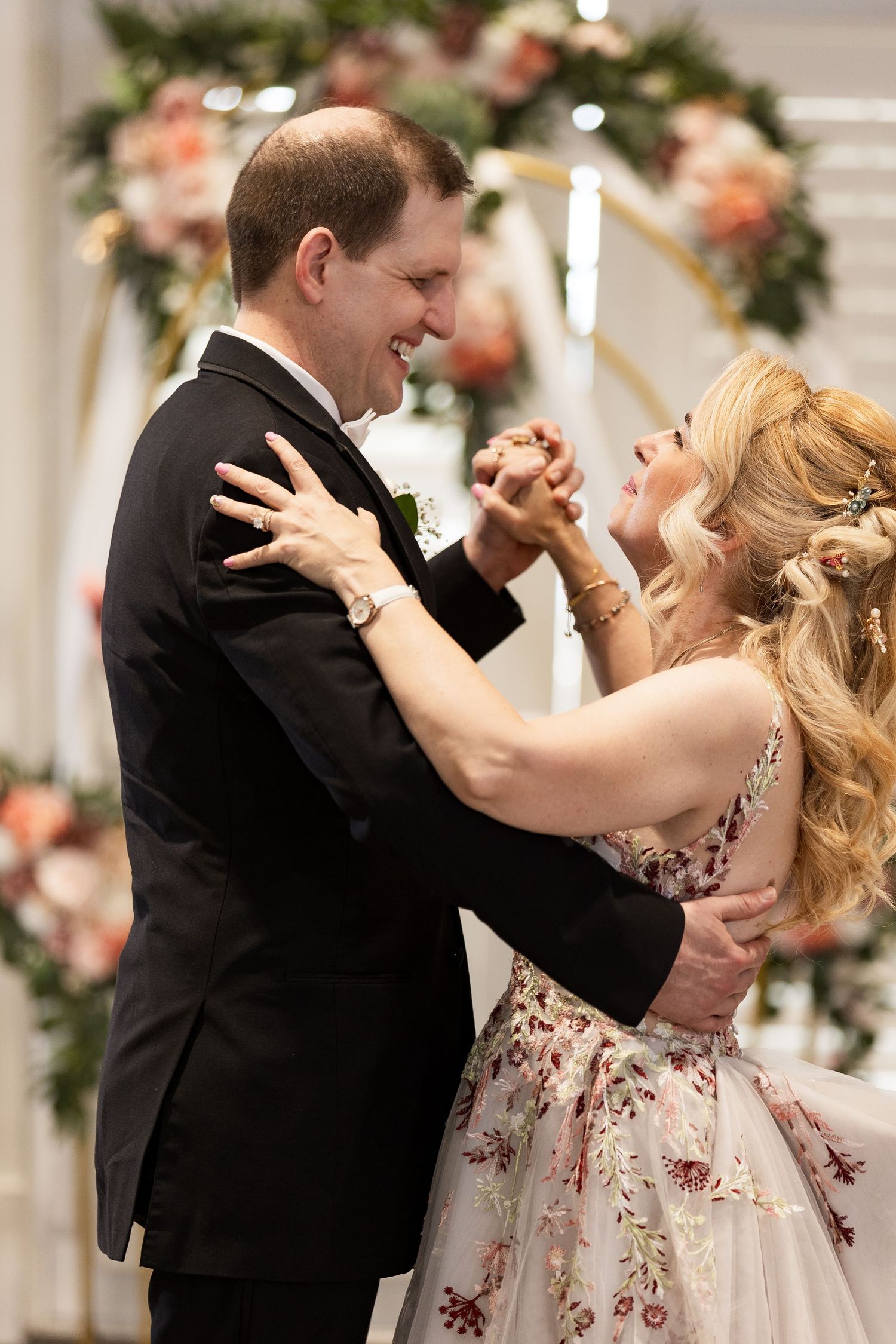 Smiling bride and groom dance together in front of a floral arch during their wedding reception.