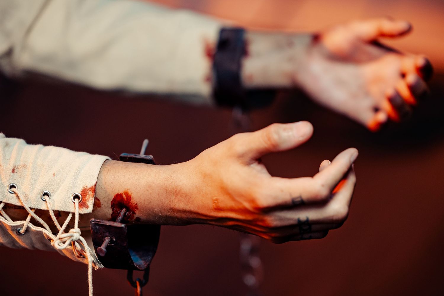 Close-up shot of bound hands with dramatic lighting showing theatrical blood effects.