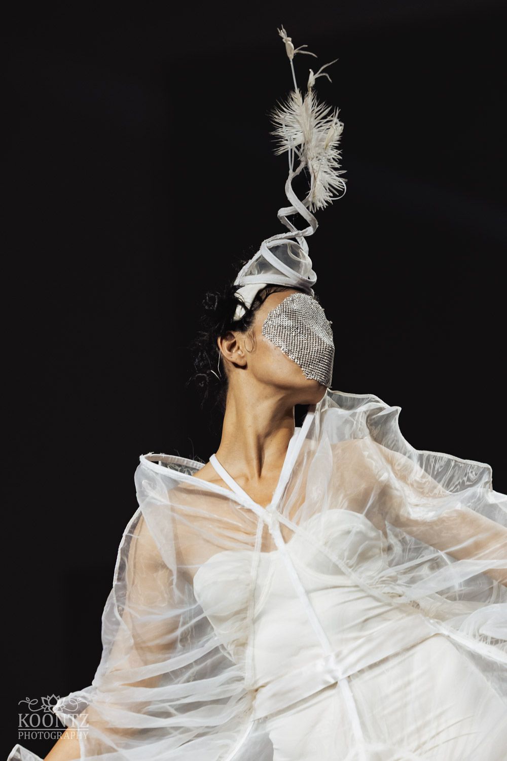 Figure in white sheer fabric against black background creating ethereal movement and dramatic dance poses.