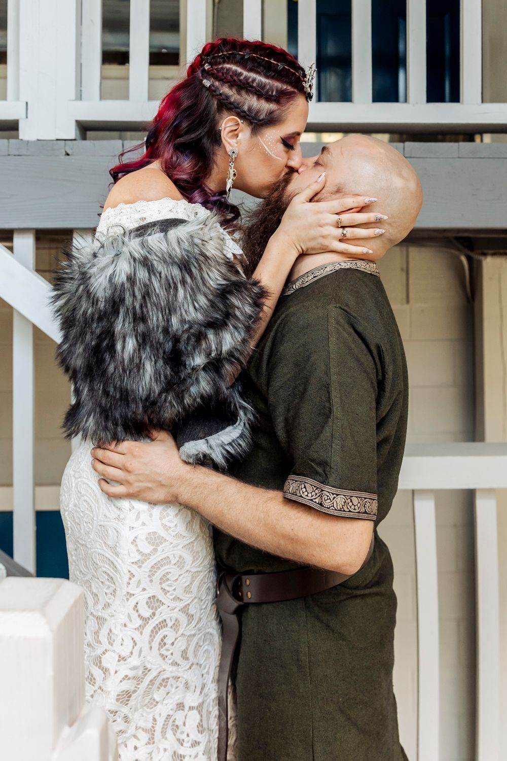 A couple shares a tender moment on stairs with one wearing a white dress and fur wrap.