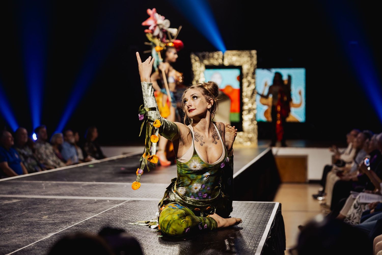 Female performer in green costume posing on runway at a creative fashion show.