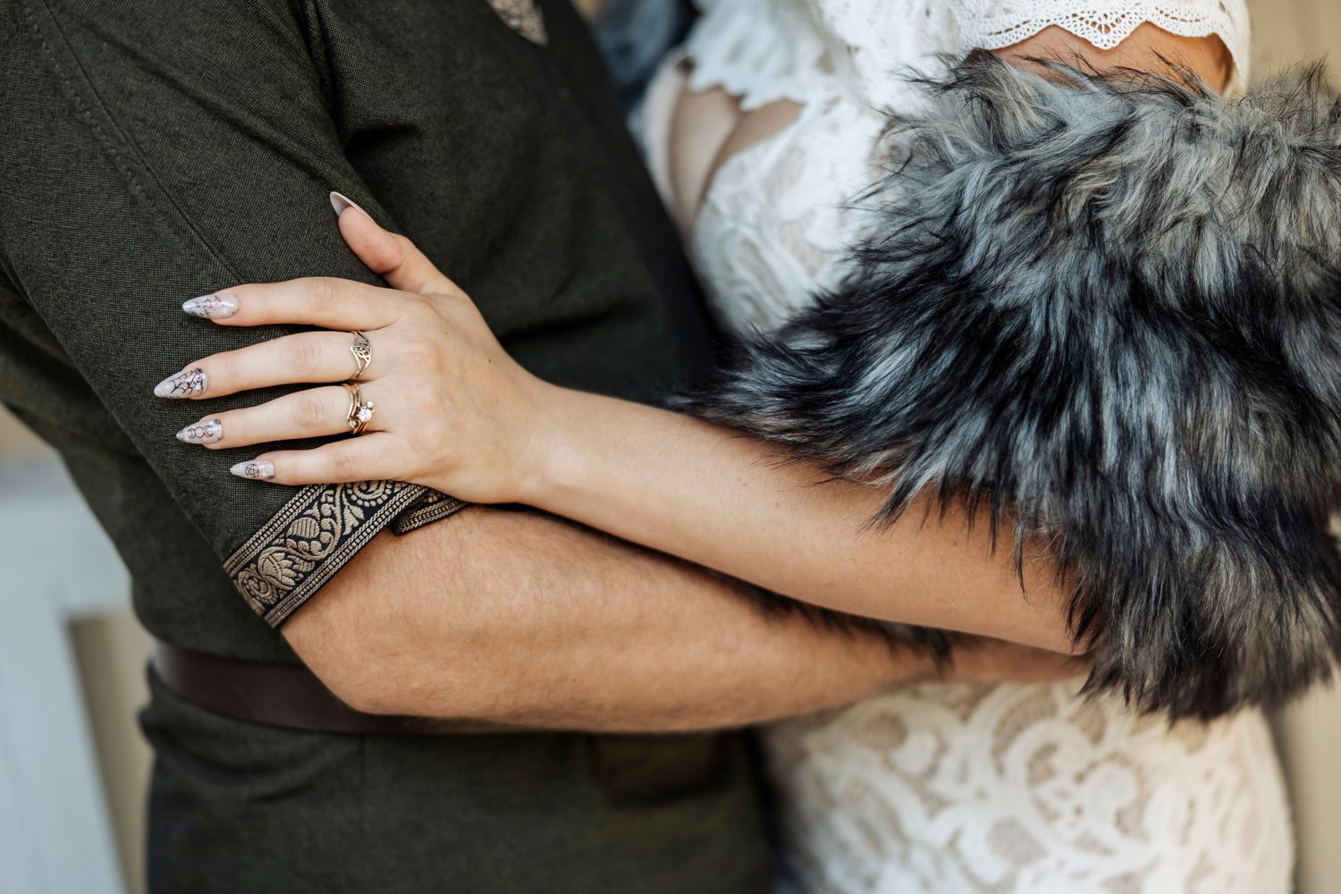 Close-up of bride and groom hands with wedding ring, she wears lace gown and gray fur wrap.