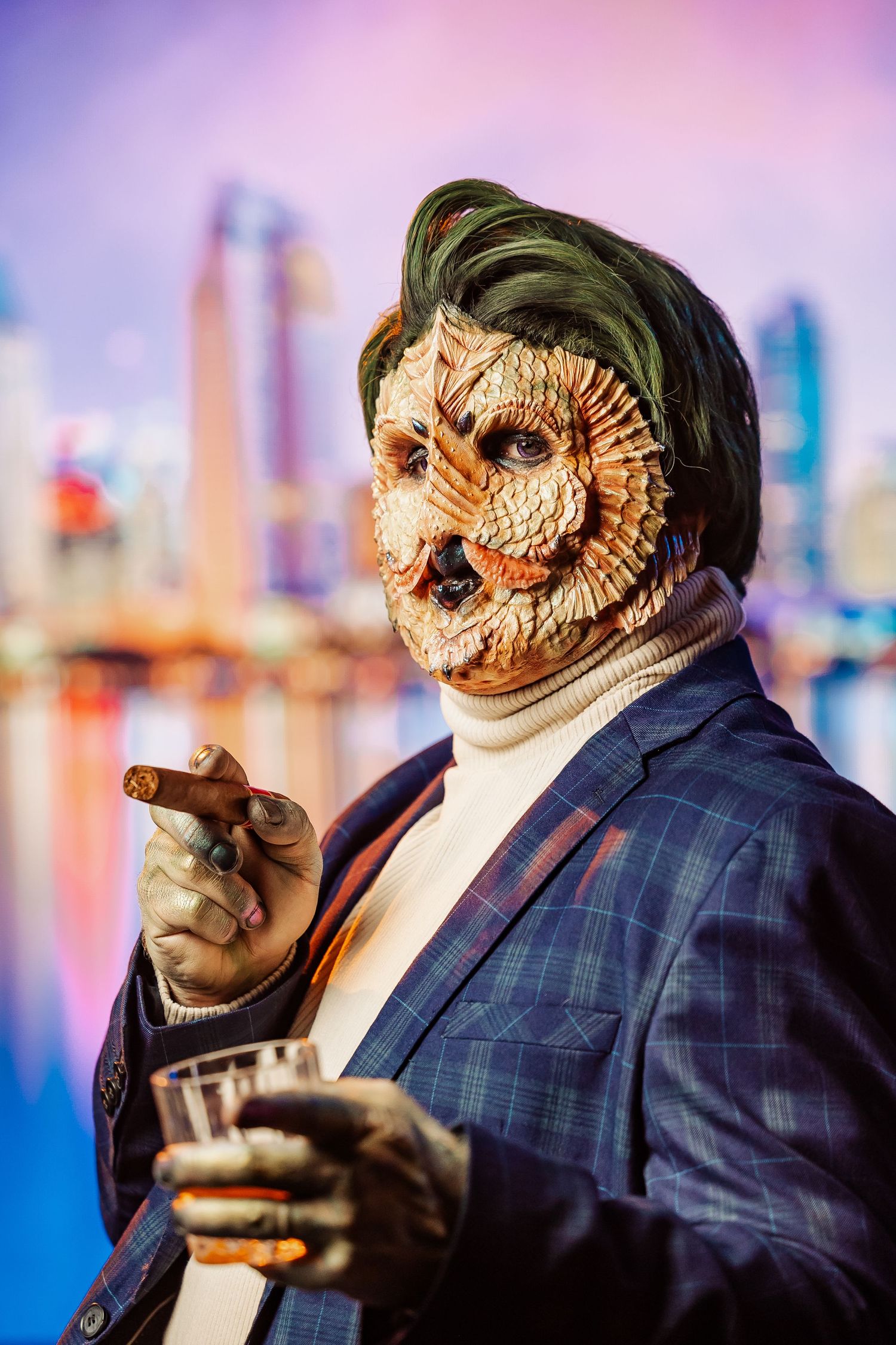 Close-up of figure wearing ornate mask and plaid suit against colorful urban backdrop.