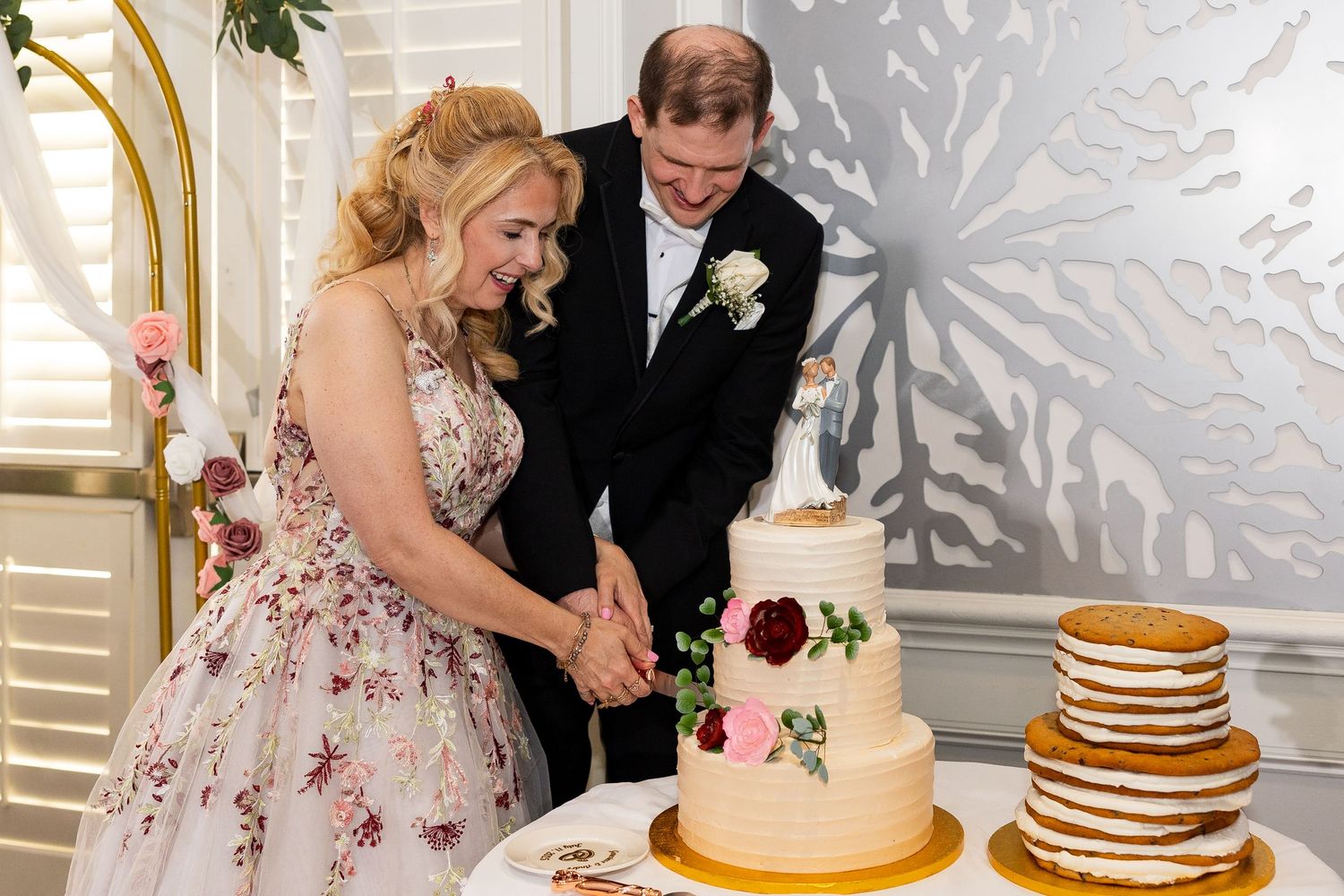 Bride and groom cut their floral-decorated white wedding cake beside a rustic naked cake.