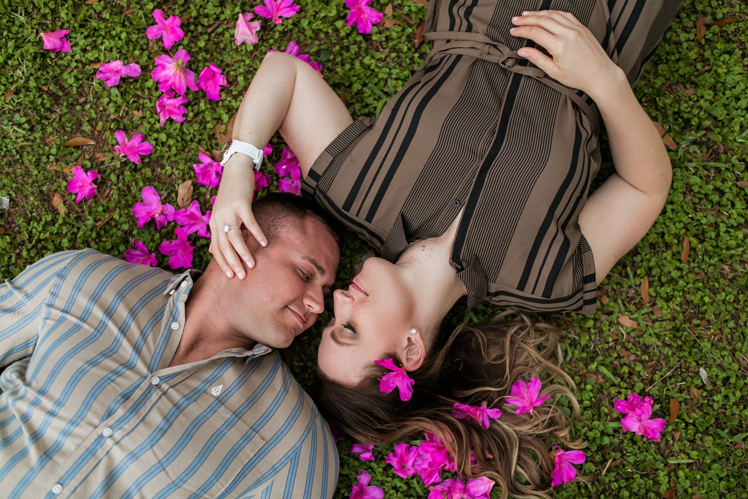 Couple lying on grass surrounded by vibrant pink flowers.