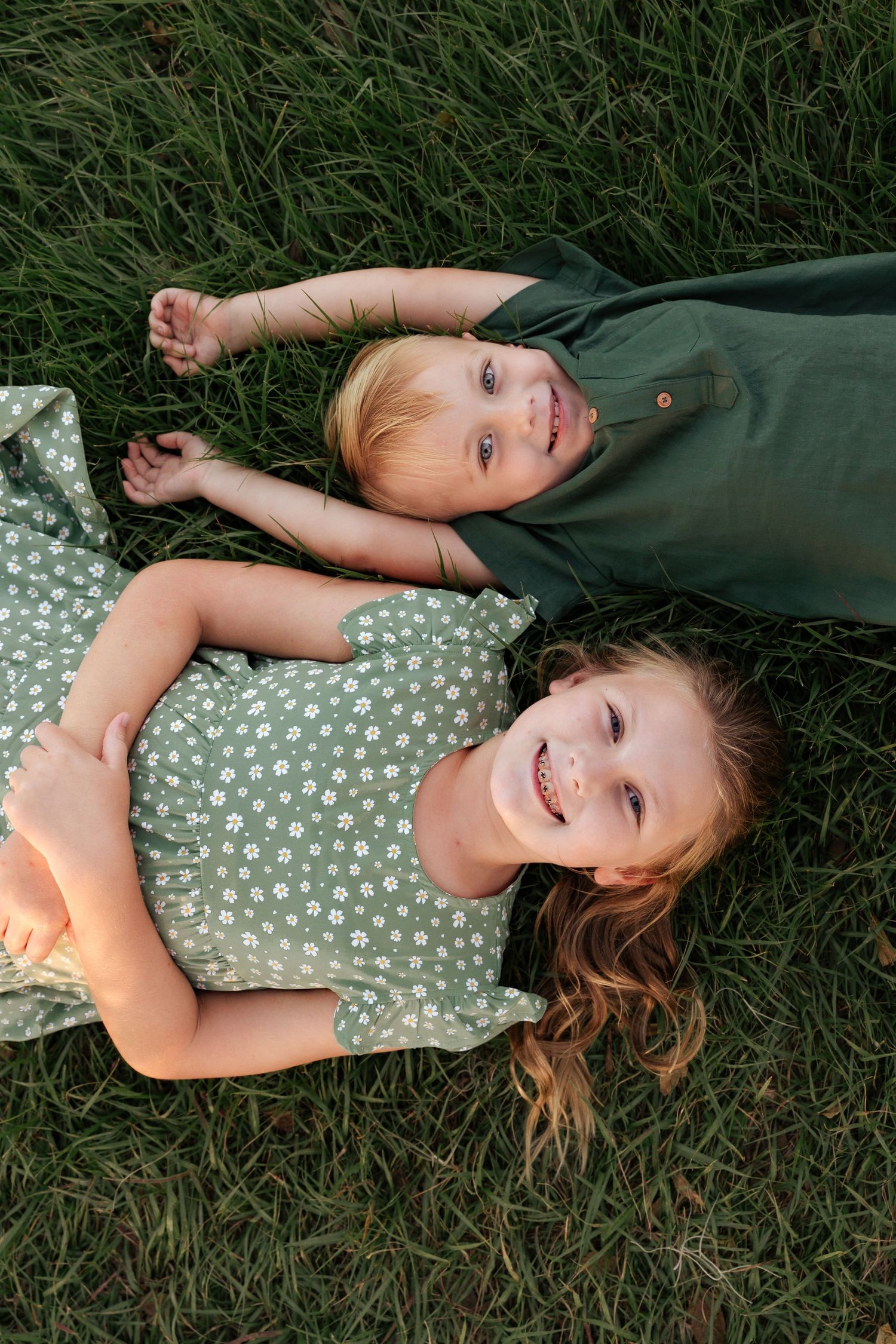 Two children lying in green grass wearing coordinating outfits.
