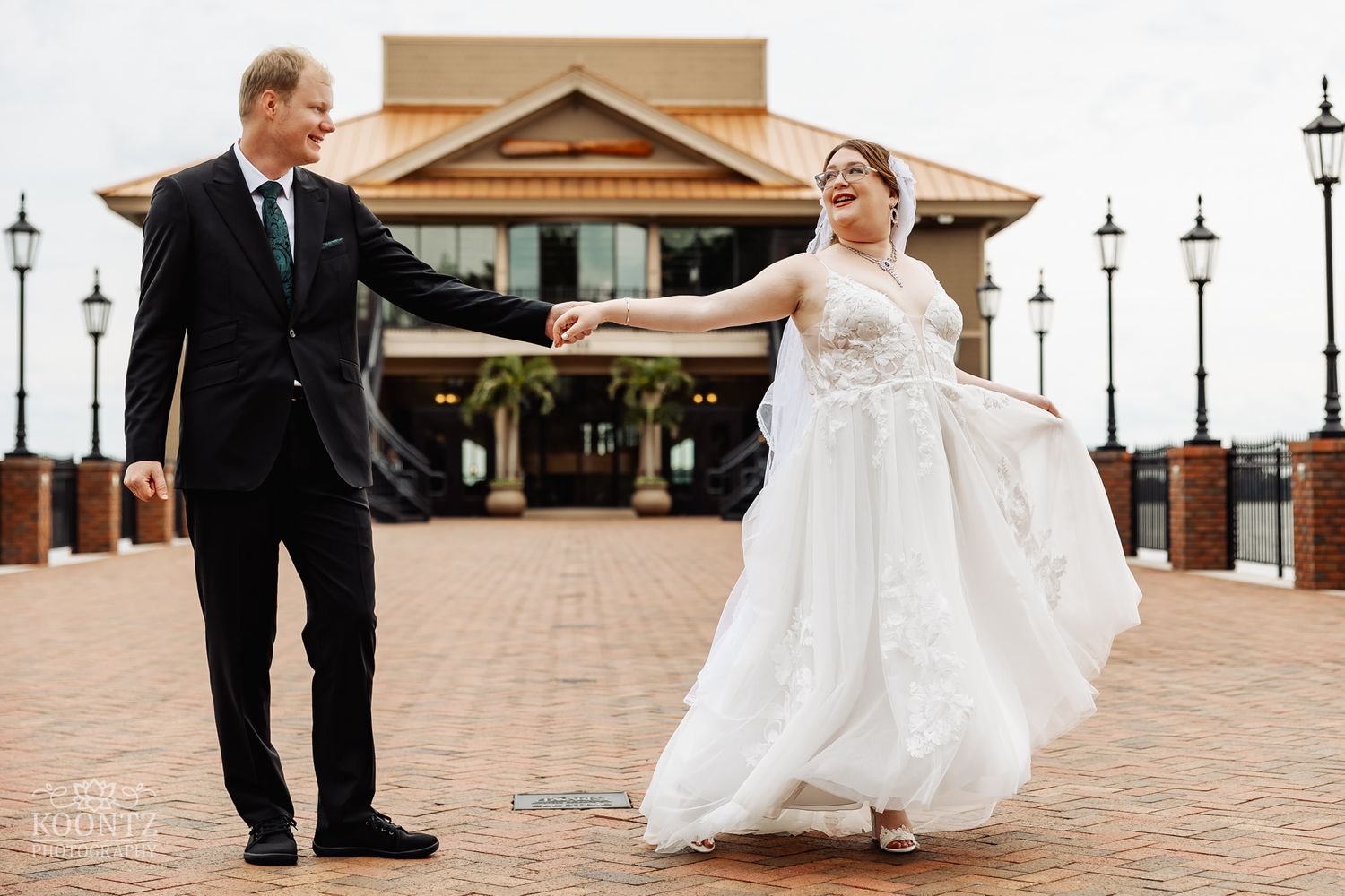 Joyful moment between couple on brick patio with Mediterranean building and lamp posts in background.