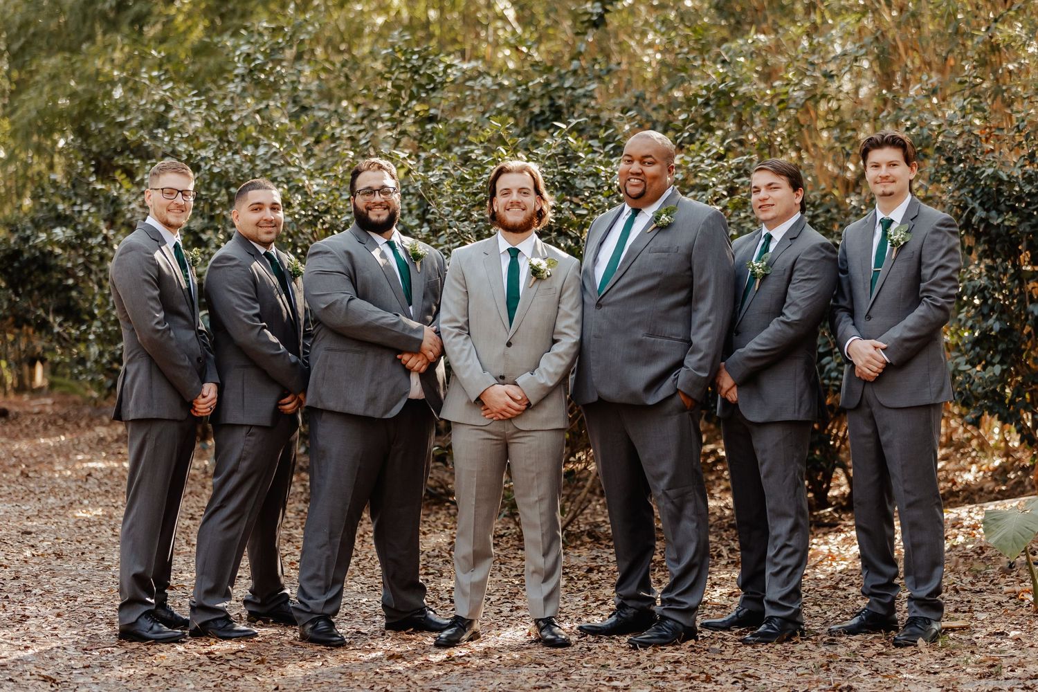 Groomsmen in gray suits posing together for formal wedding party portrait outdoors.