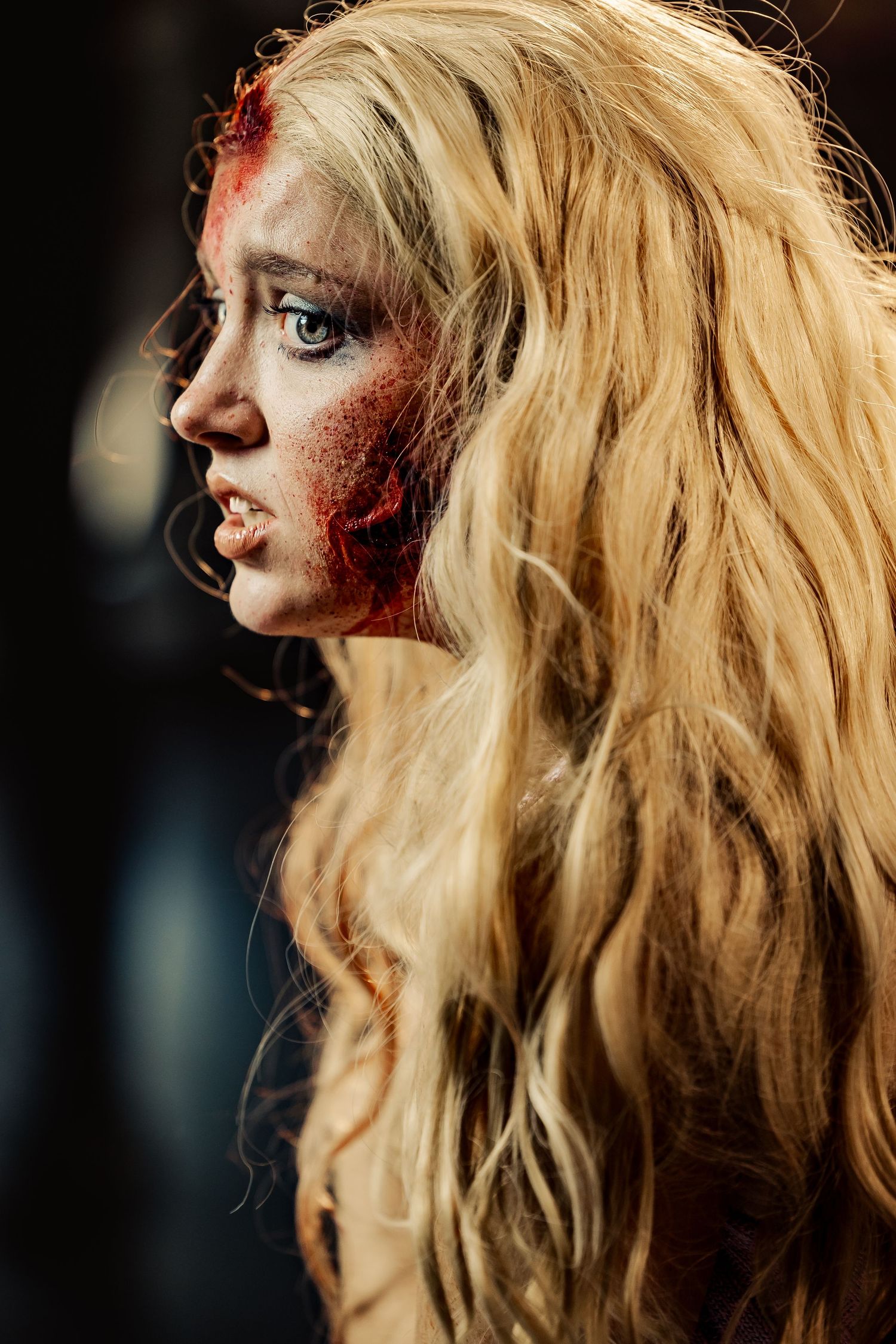 Side profile of woman with long blonde hair and realistic zombie wound special effects makeup.
