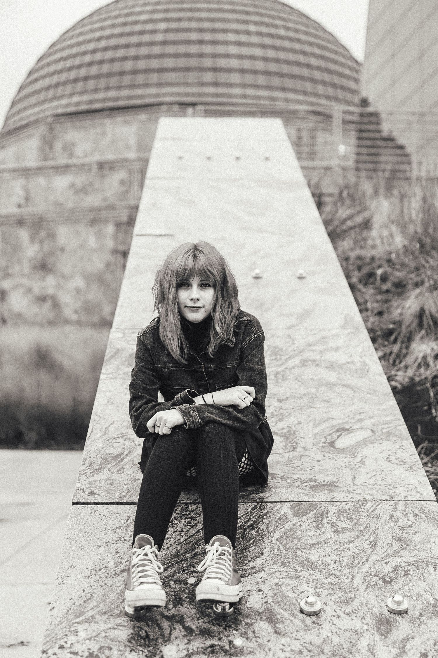 Black and white photo of a young girl sitting on a marble ledge wearing sneakers and dark clothing outdoors.