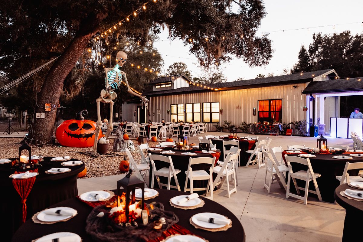 Halloween-themed outdoor wedding reception with skeleton decorations, jack-o-lanterns, string lights, and elegantly set black tables.