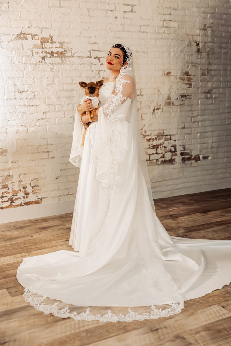 A stunning bridal portrait session featuring a flowing white wedding gown with lace details against a rustic brick wall.