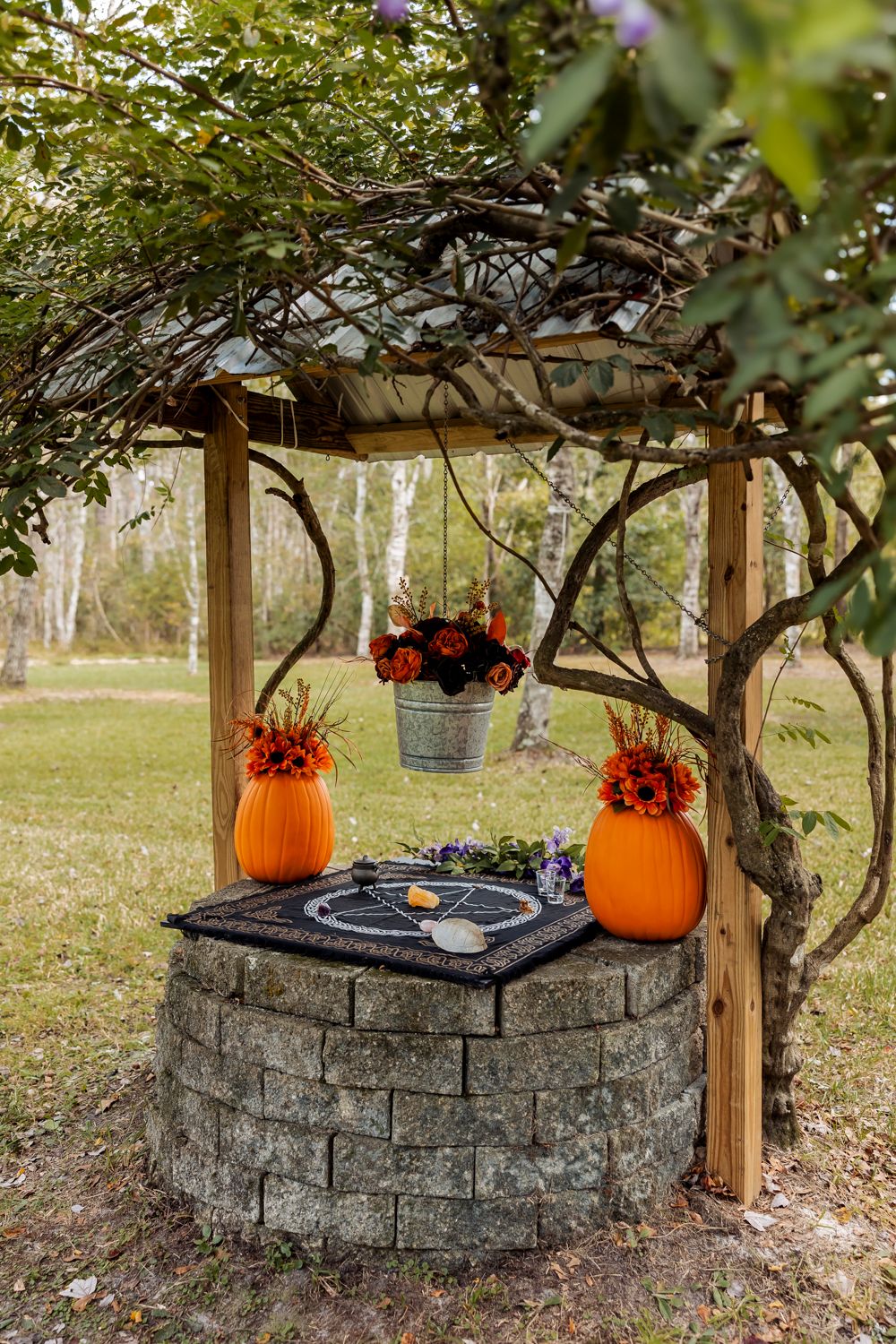 Rustic stone wishing well decorated with orange pumpkins and fall flowers.